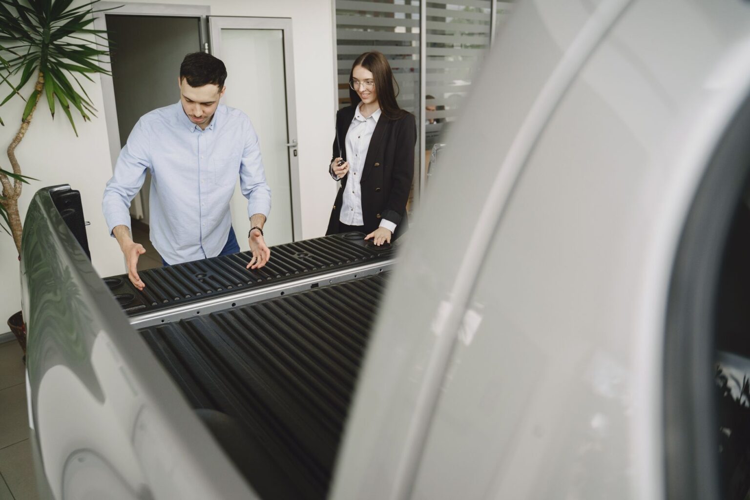 Salesman and client inspecting a pickup truck in a car dealership, discussing features.