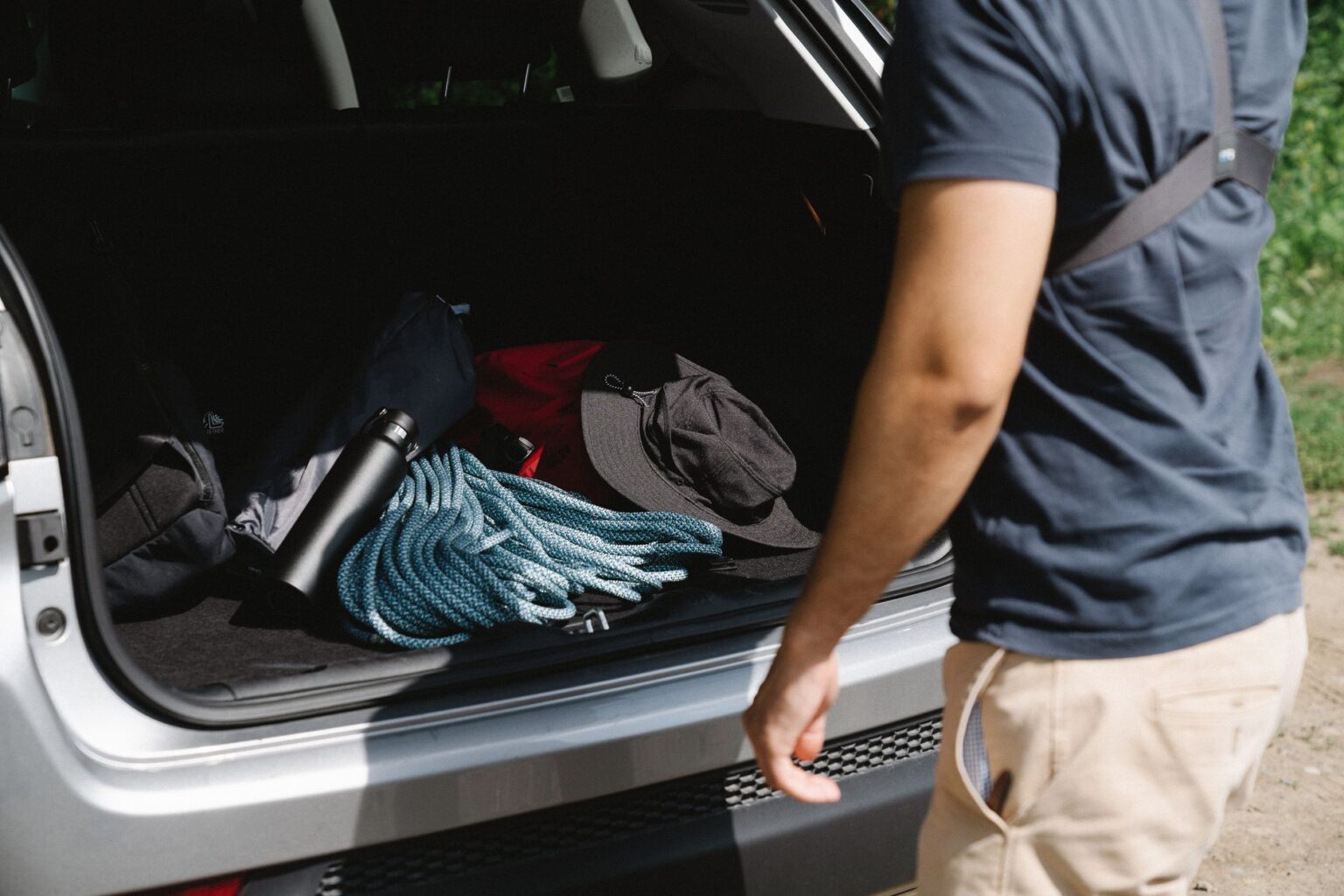 Man organizing camping gear in car trunk, ready for adventure.