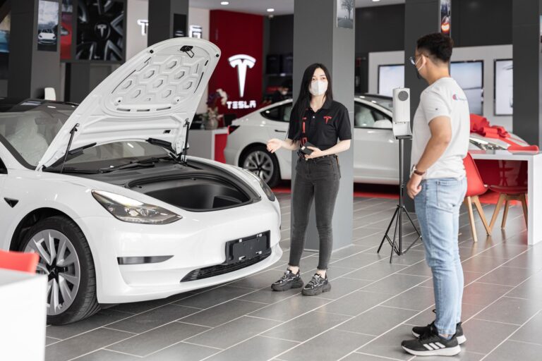 A customer talks with a sales representative about a Tesla Model 3 in a car dealership.