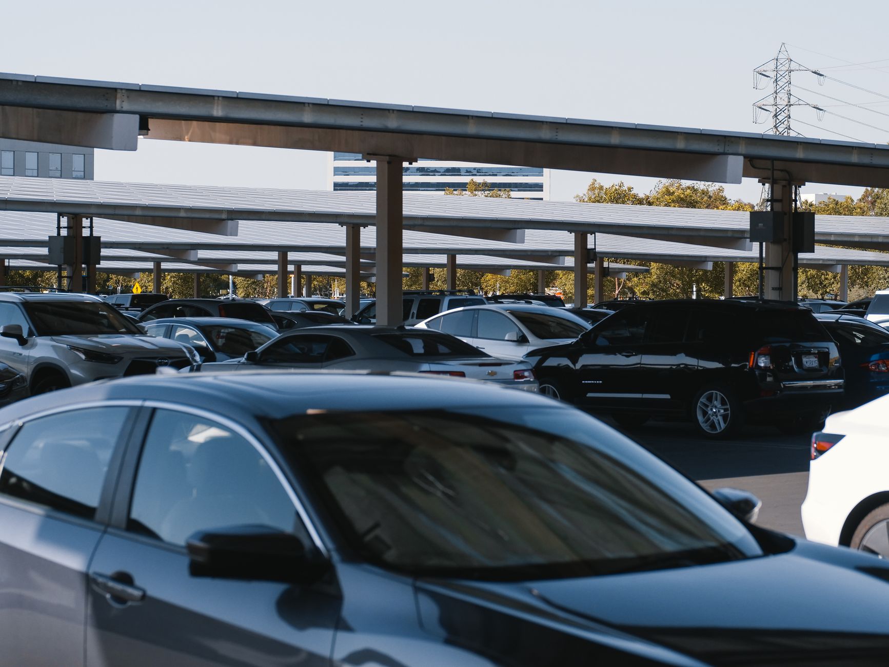 A busy outdoor parking lot filled with various parked cars under solar panel structures.