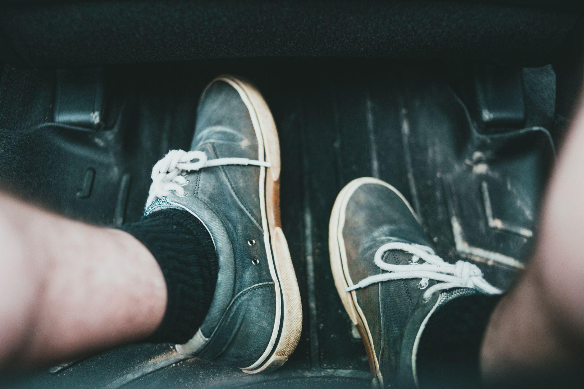 Close-up view of casual sneakers on a car's floor mat, highlighting footwear style and interior setting.