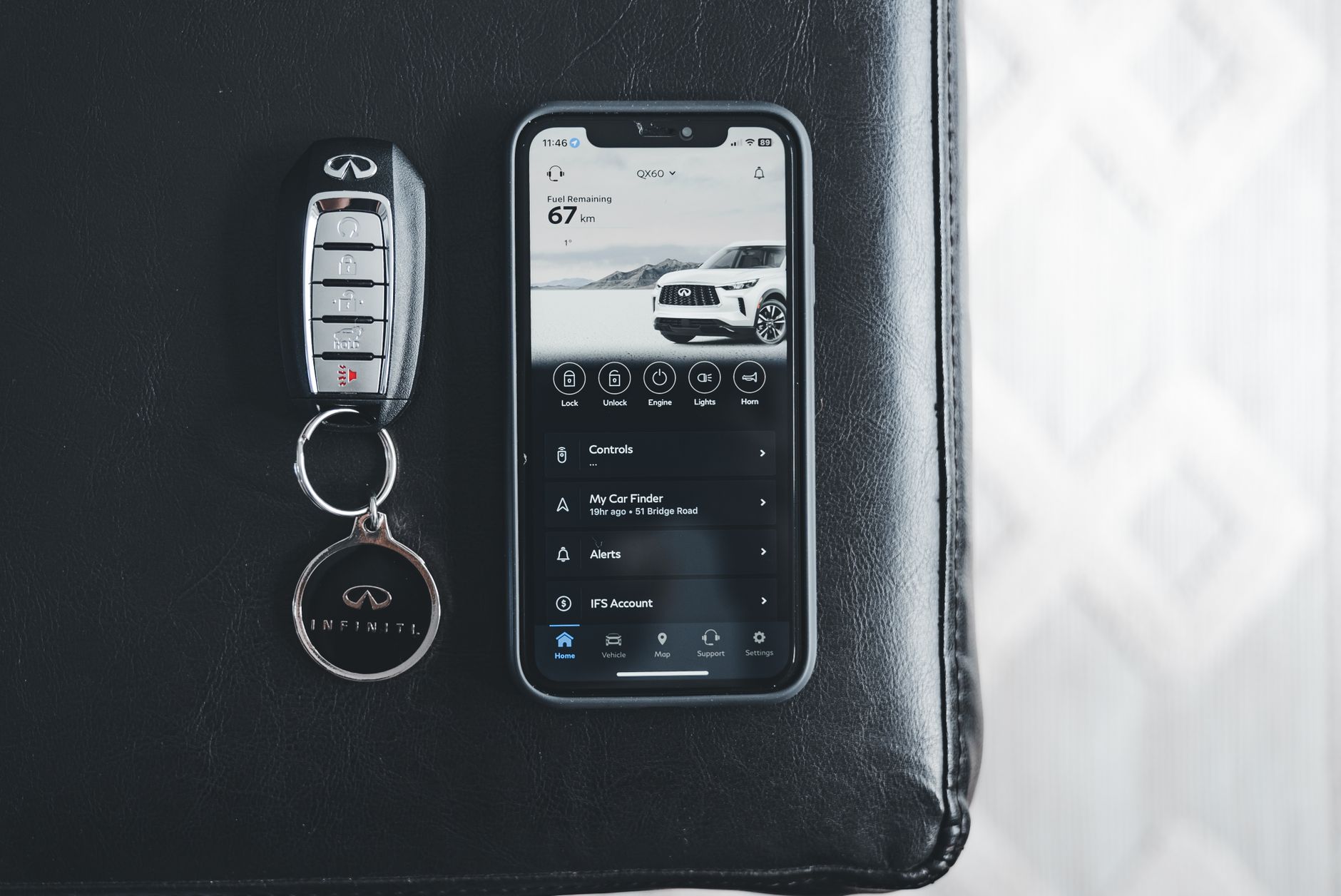 Close-up of a key fob and smartphone displaying a car app on a leather surface.