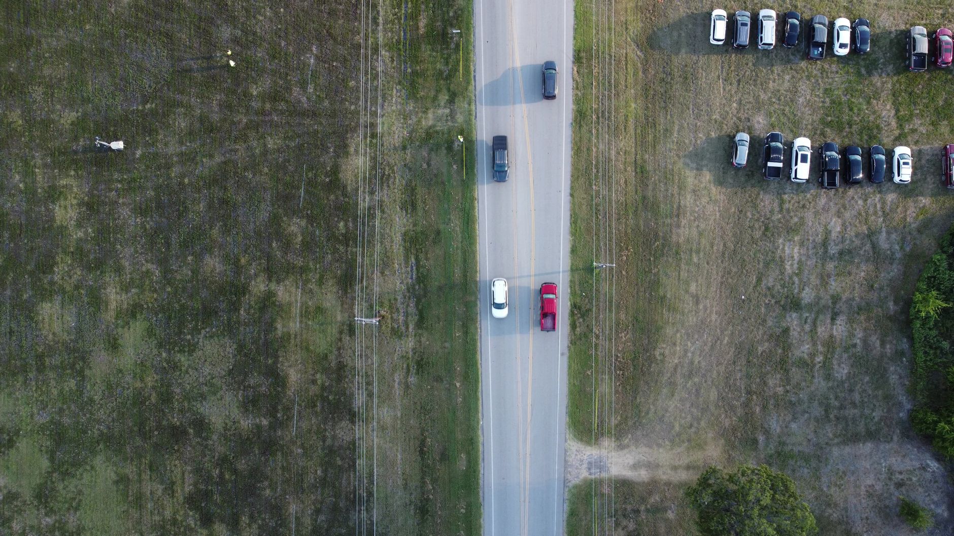 Drone shot capturing cars and parked vehicles along a rural road in Texas.