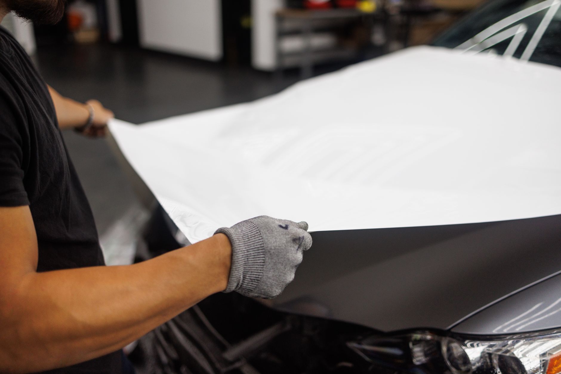 Person applying vinyl wrap to a car hood in a garage.