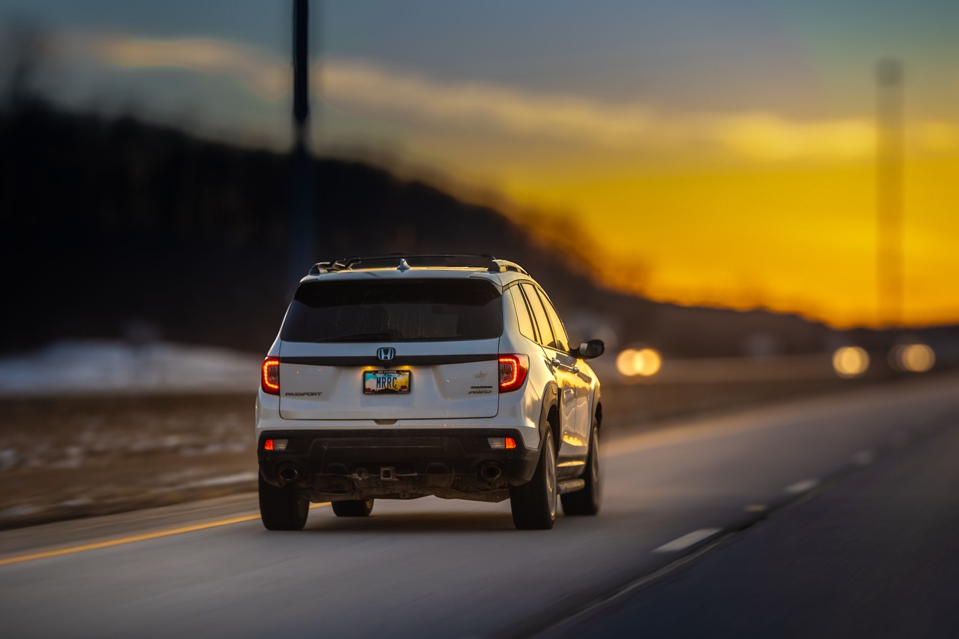 A white SUV traverses an empty highway during sunset, with a vibrant sky and dynamic motion blur.