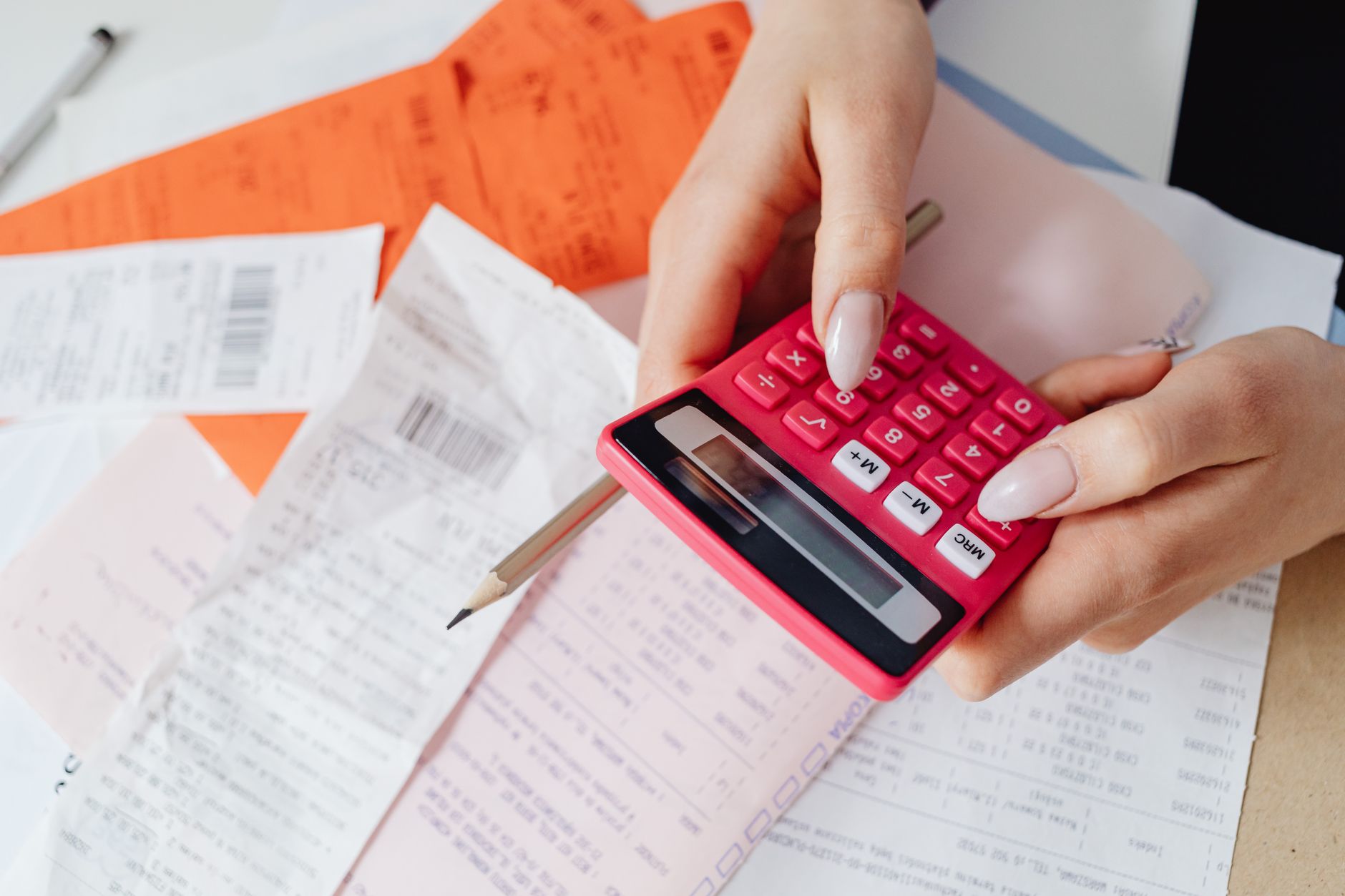 Hands using a calculator to manage expenses amidst various receipts and documents.