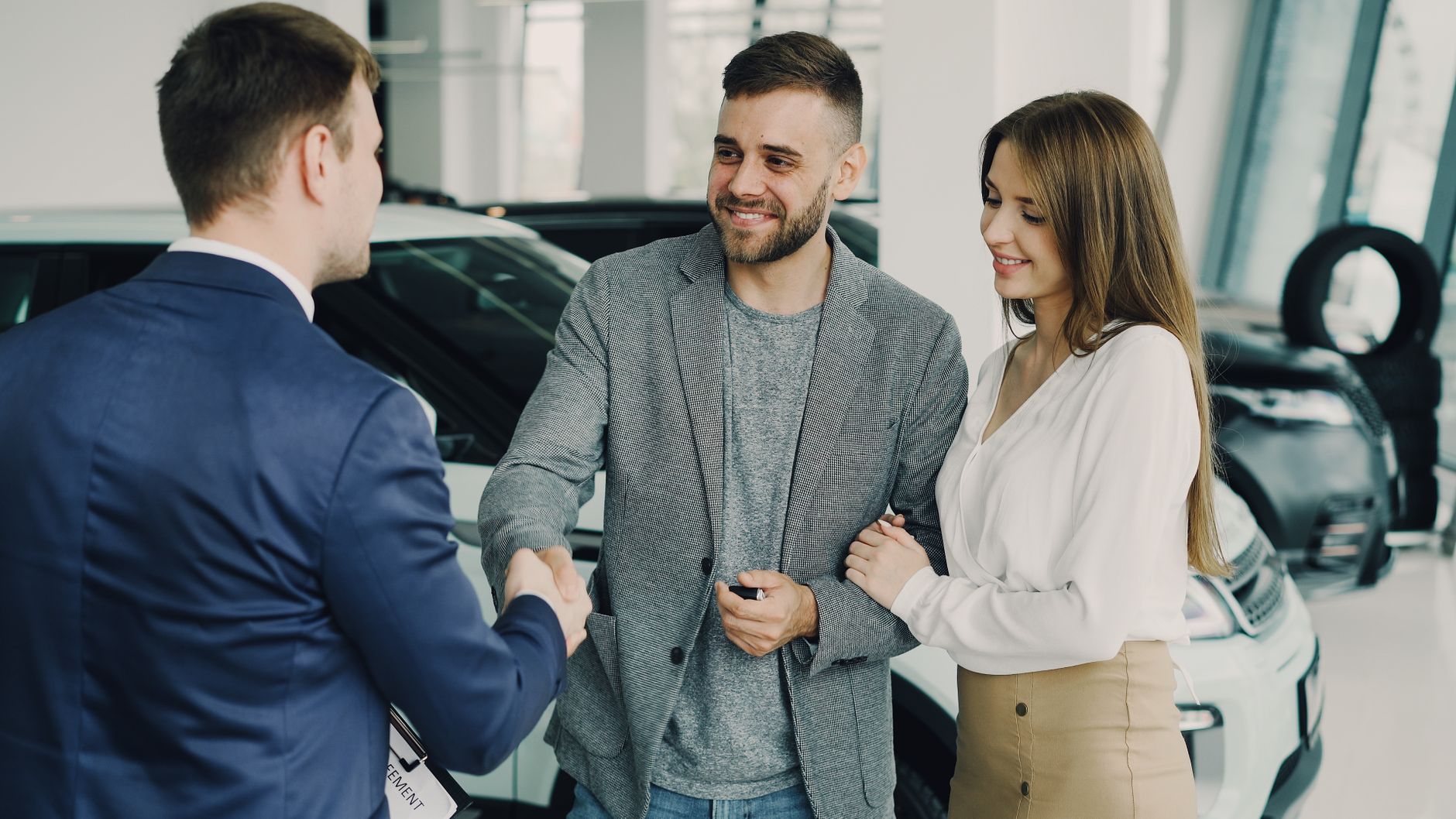 Happy couple finalizing car purchase with salesman in dealership showroom.