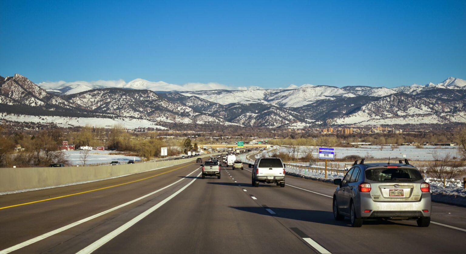 A scenic highway view surrounded by snow-capped mountains under a clear blue sky, showcasing traffic flow in Colorado.
