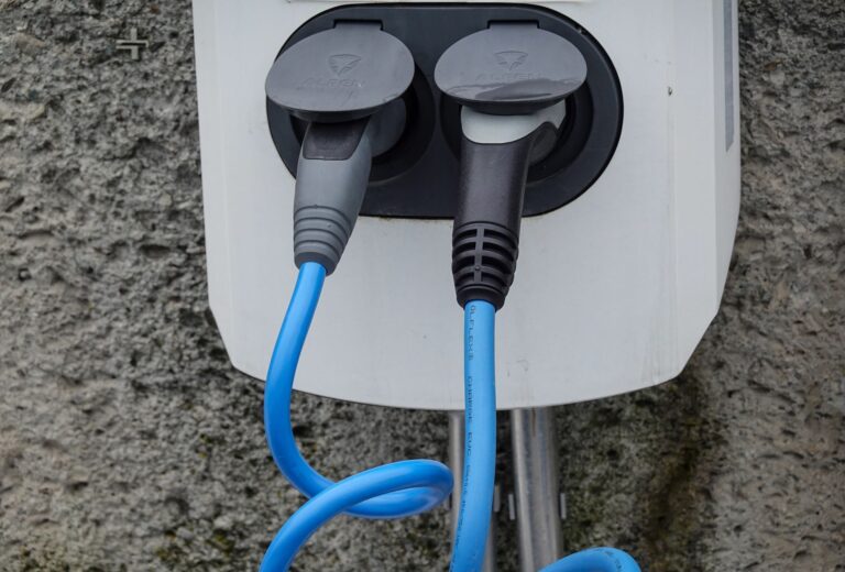Close-up of an electric vehicle charging station with two cables in sockets against a textured wall.