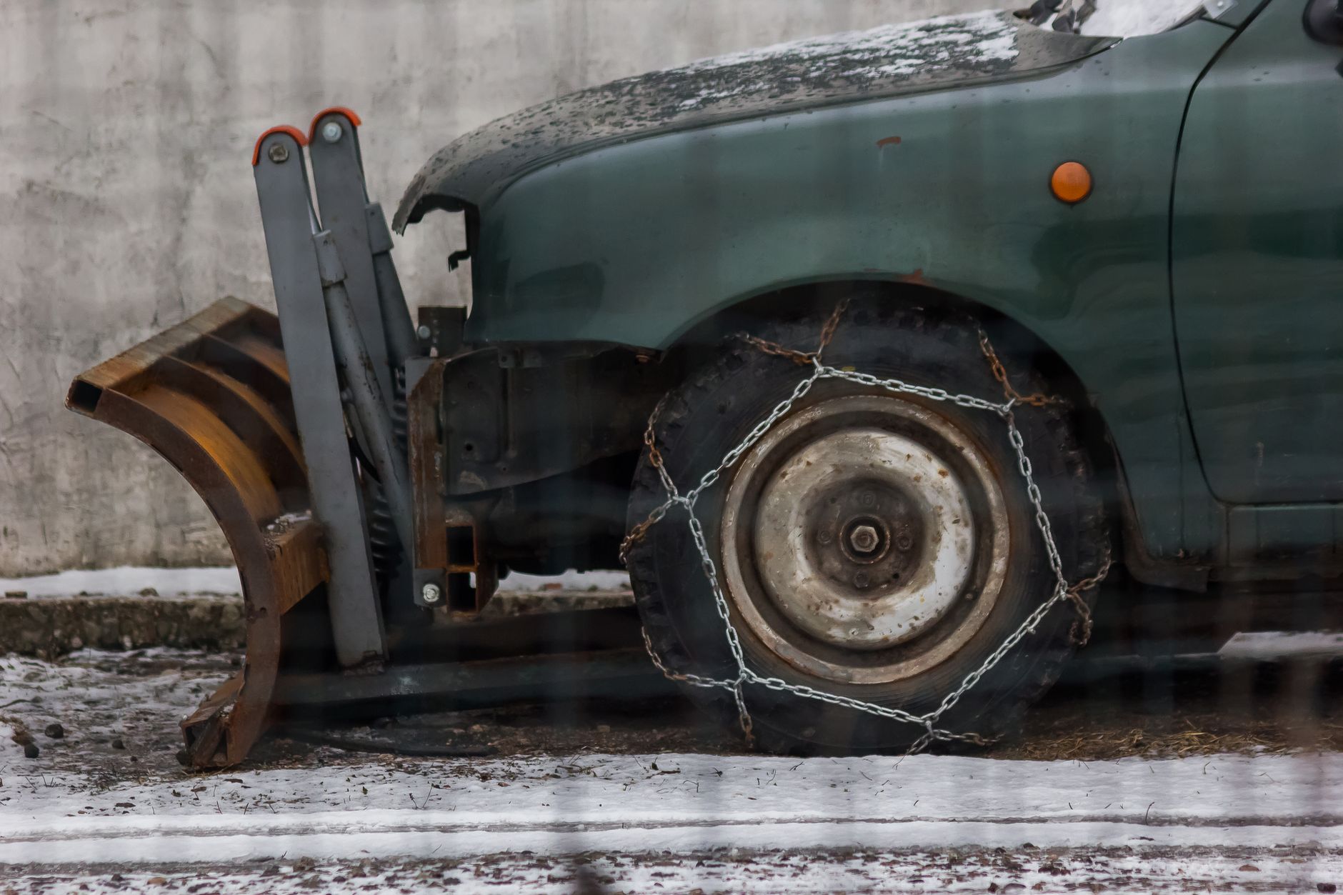 Close-up of a parked snowplow vehicle with chains on tires, ready for winter conditions.