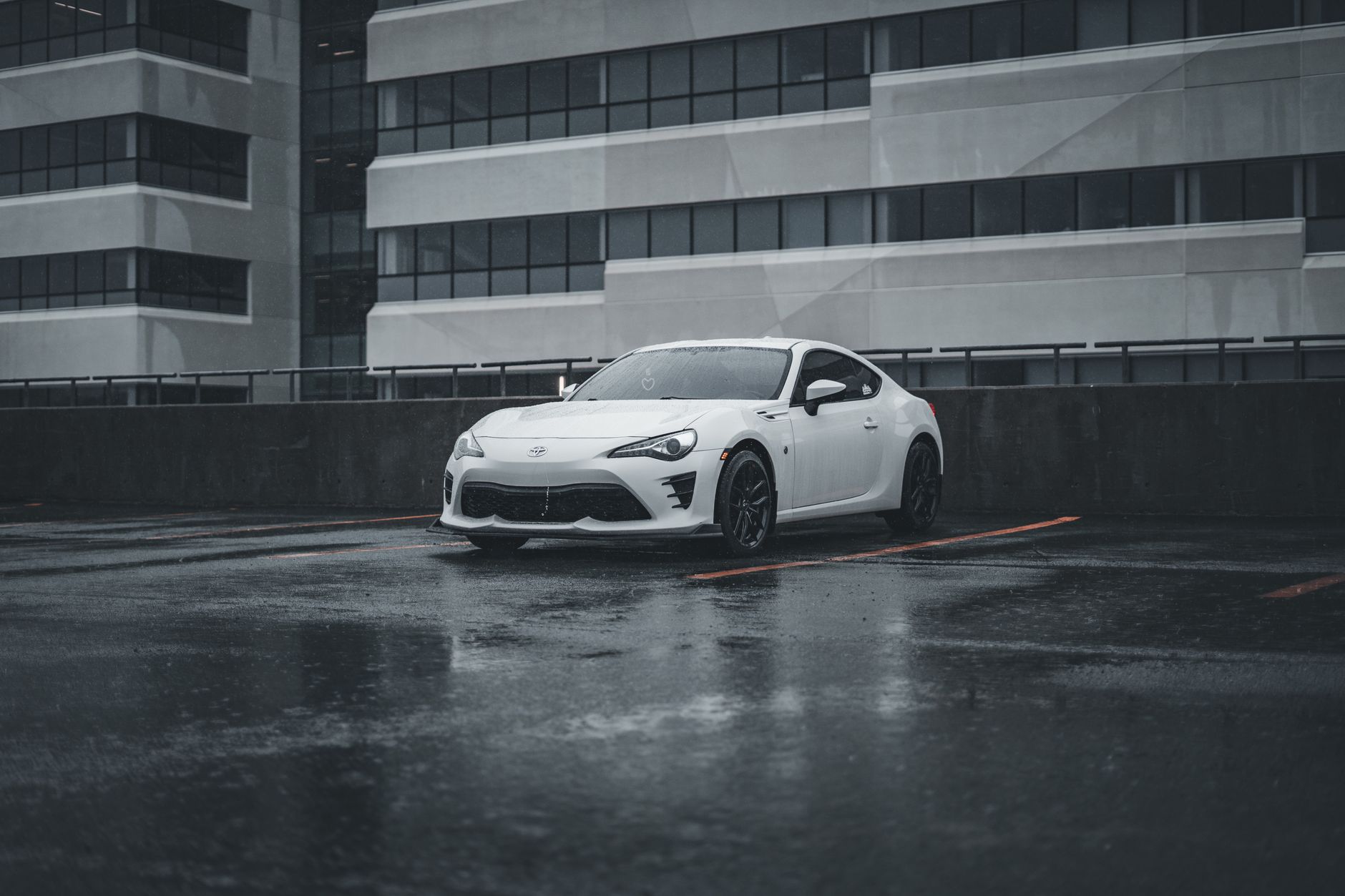 A sleek white sports car parked in a rainy cityscape, showcasing modern urban architecture.