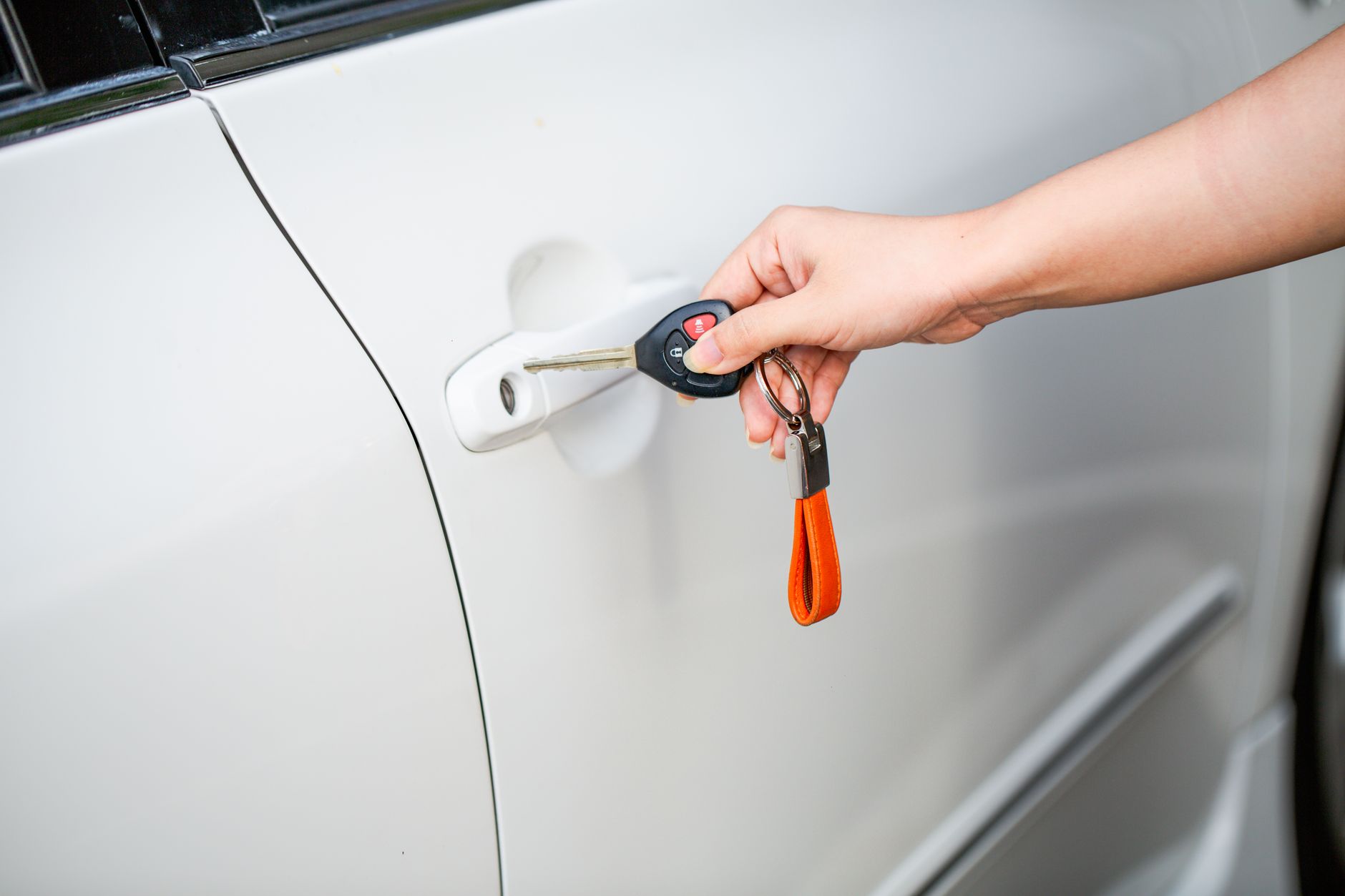 Close-up of a hand unlocking a car door with a key and key fob