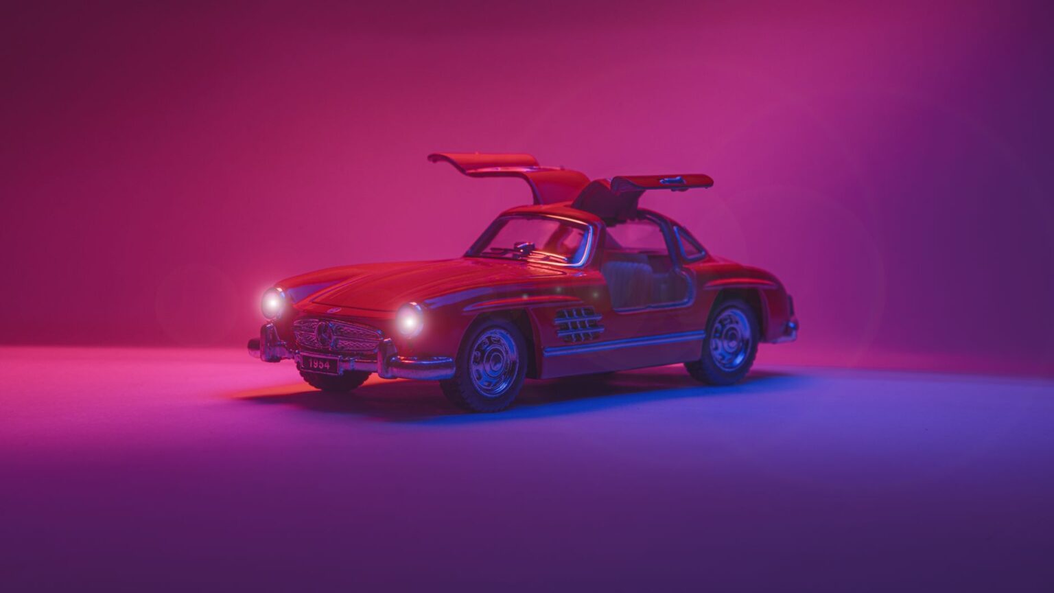 A striking red classic sports car with open gullwing doors under vibrant studio lighting.