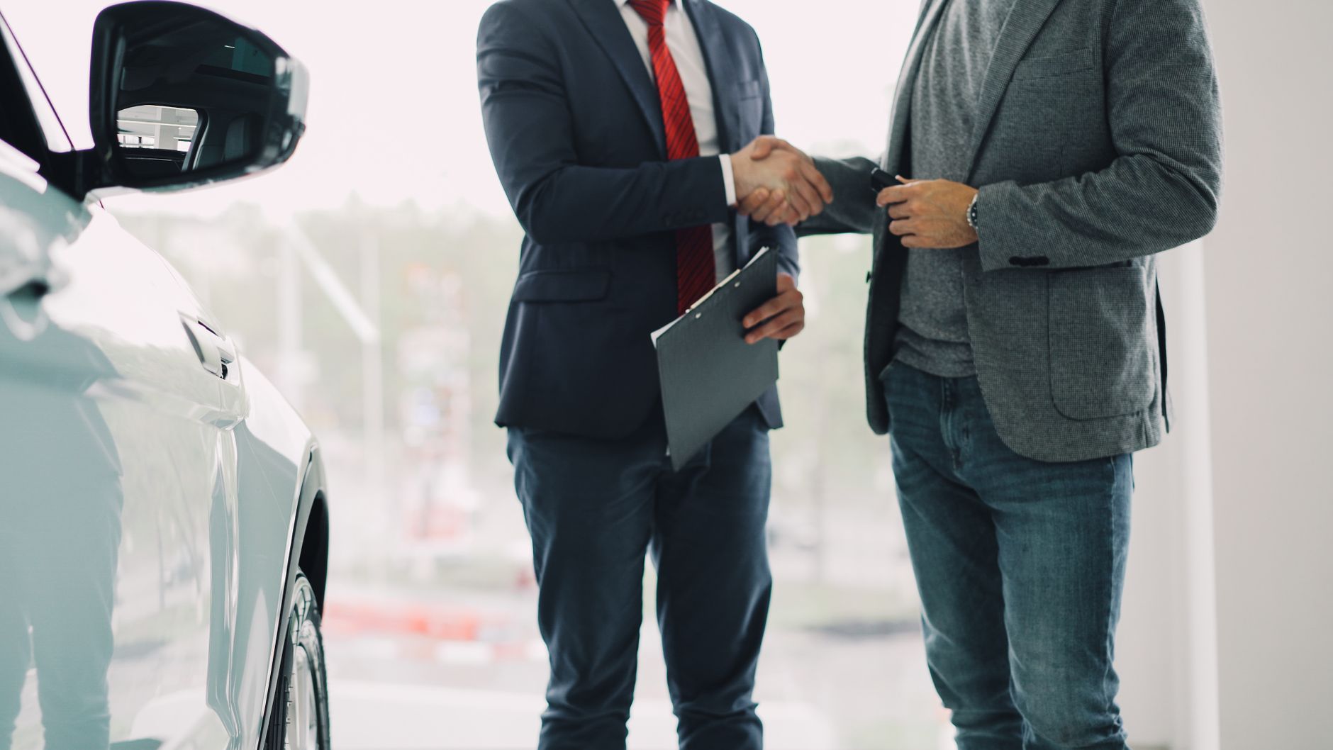 Two men shake hands in a car dealership, sealing a business deal.