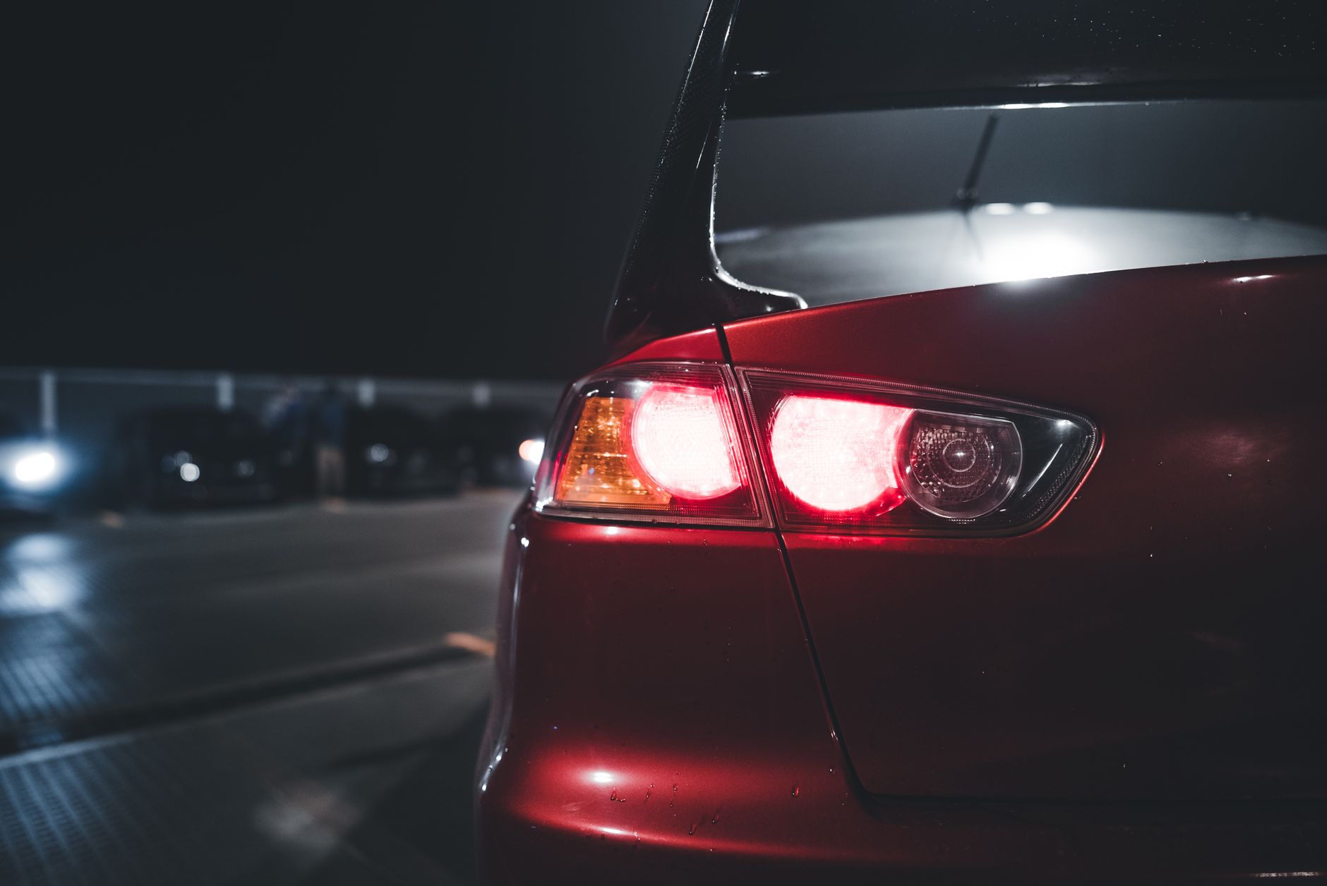 Close-up of a red sports car with a spoiler in a dimly lit parking lot at night.