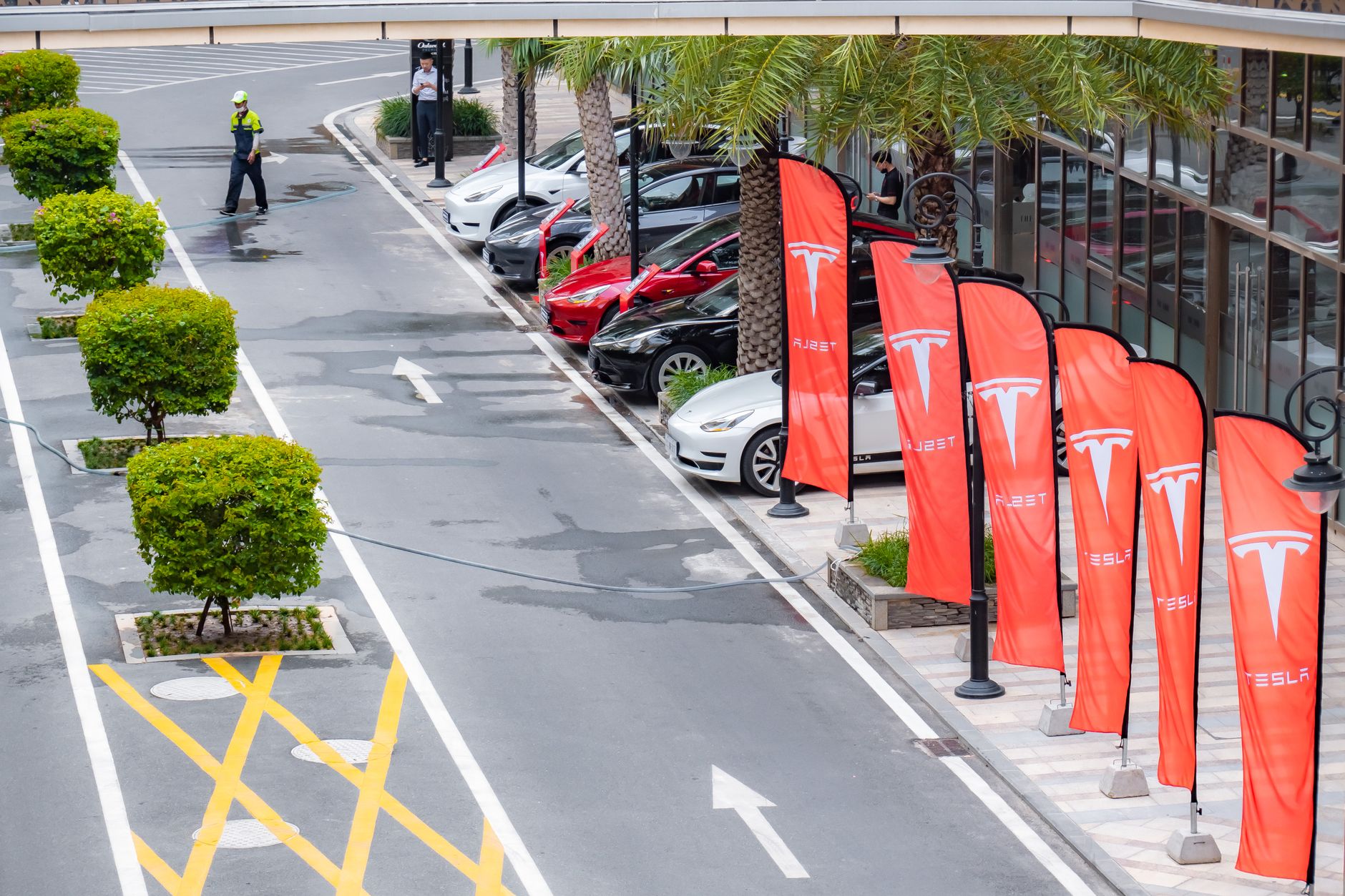 Aerial view of multiple Tesla cars parked alongside branded flags in a city street.