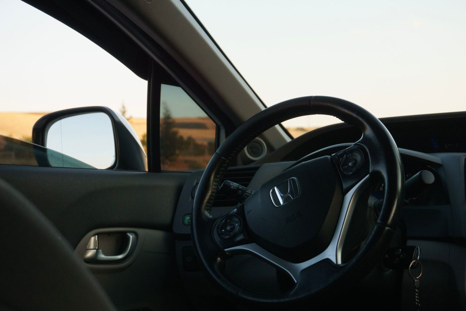 Close-up of a car steering wheel with dashboard and window view, embodying luxury and travel.