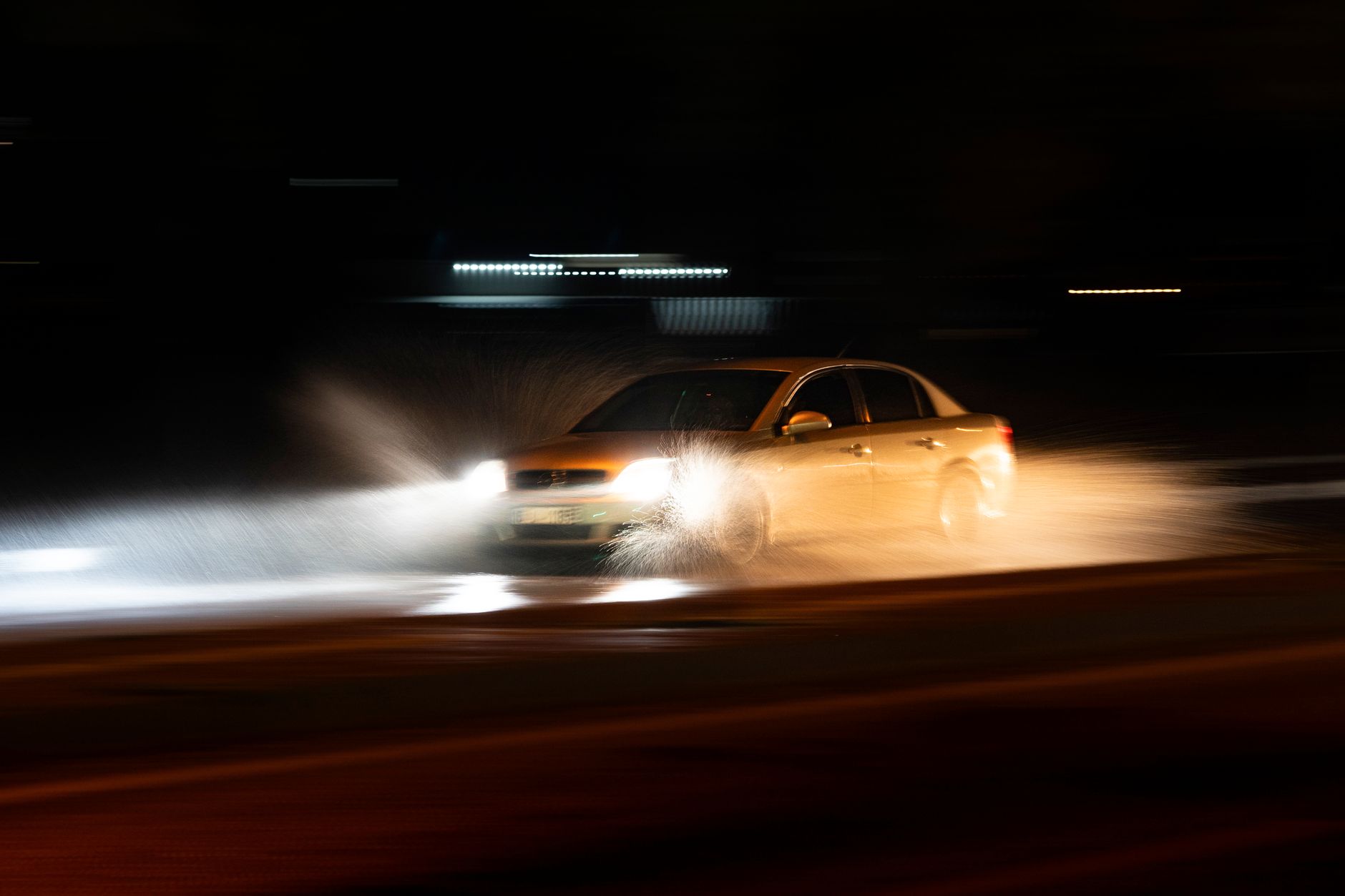 A car speeding through a wet road with dramatic splashes during a nighttime drive.