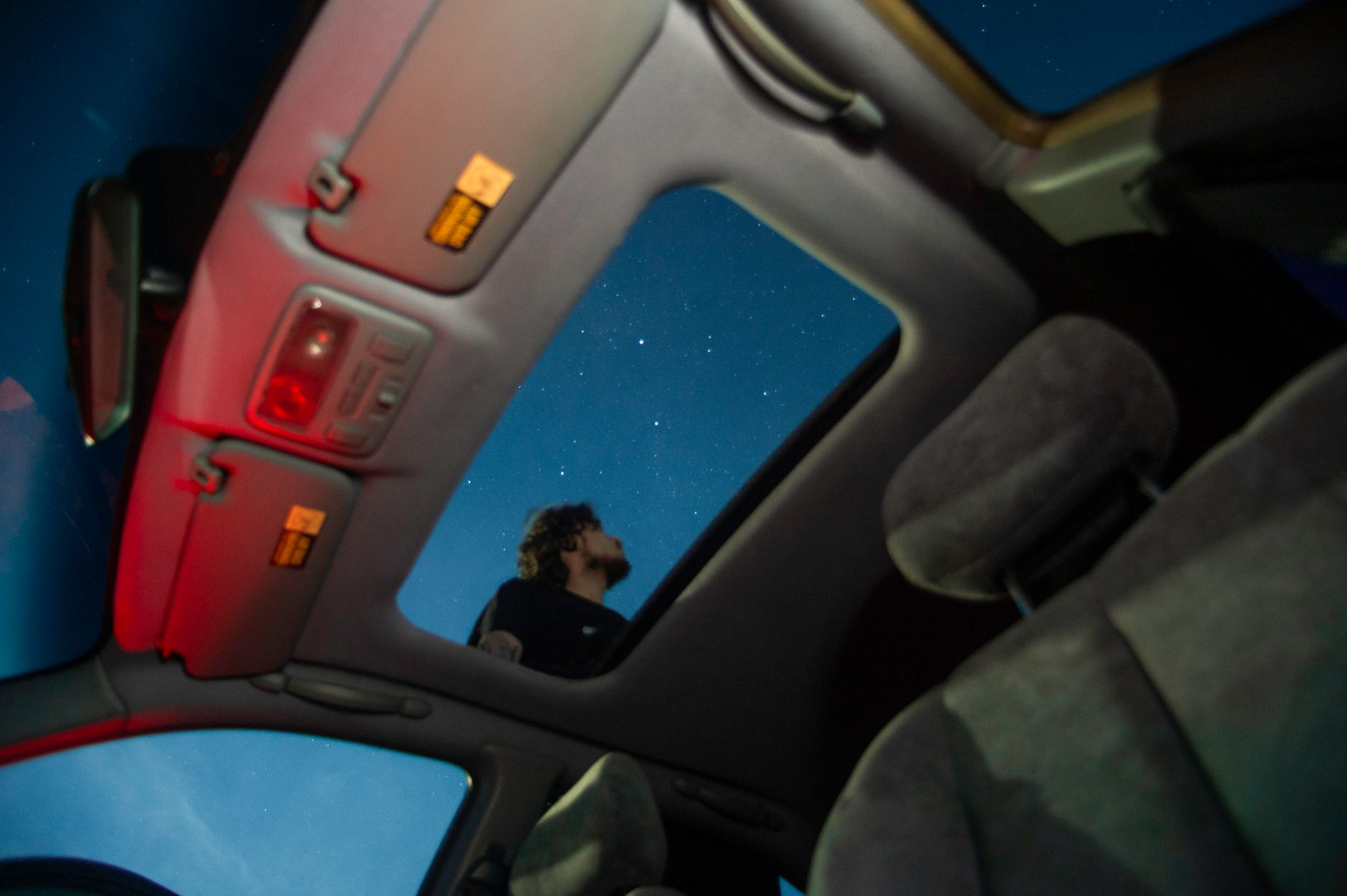 Man stargazing through car sunroof, capturing a serene night sky with stars.