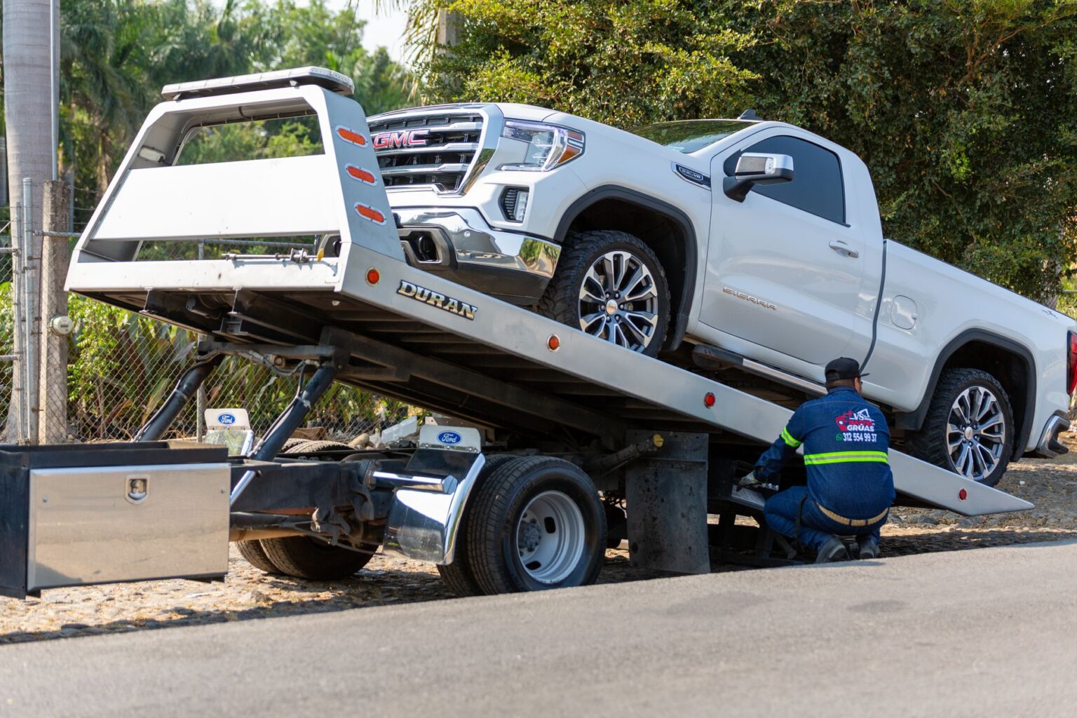 Tow truck operator loading a pickup truck on a flatbed in daytime.