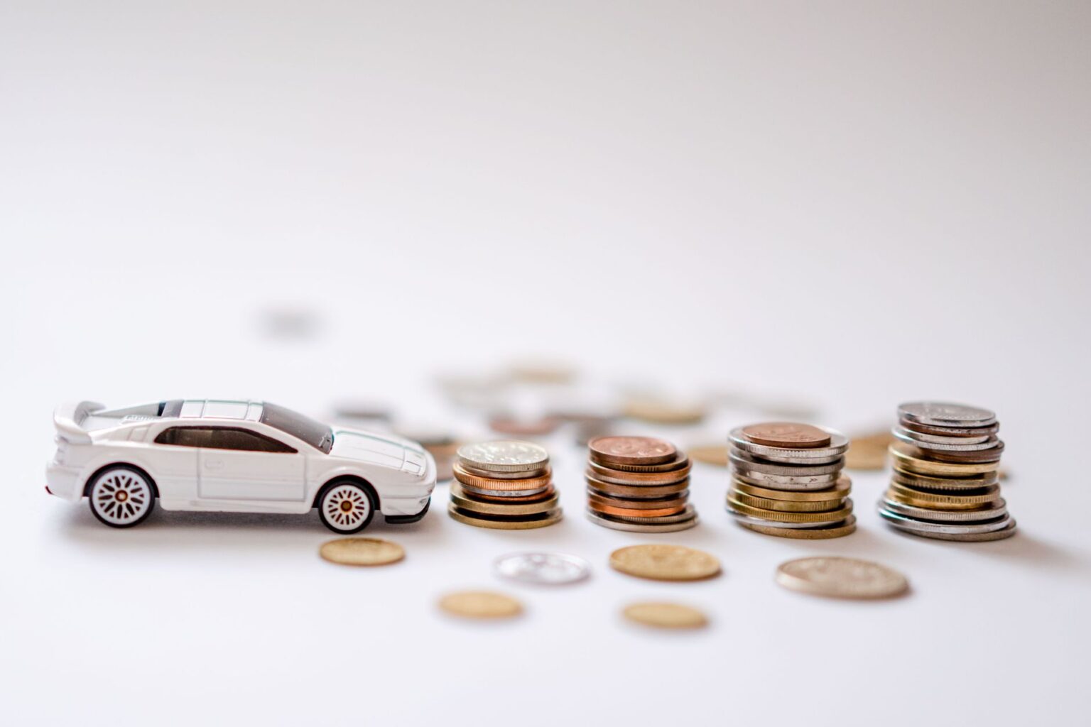 White toy sports car beside stacks of coins, emphasizing savings and finance